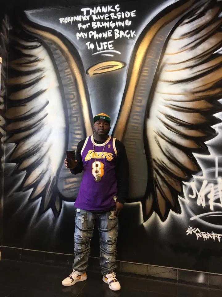Man in Lakers jersey stands in front of a wing mural with a “thanks for bringing my phone back” message above.