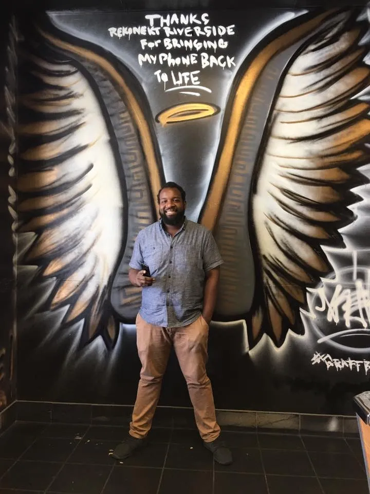 Man stands in front of a mural of angel wings and a halo with text thanking someone for returning a phone.